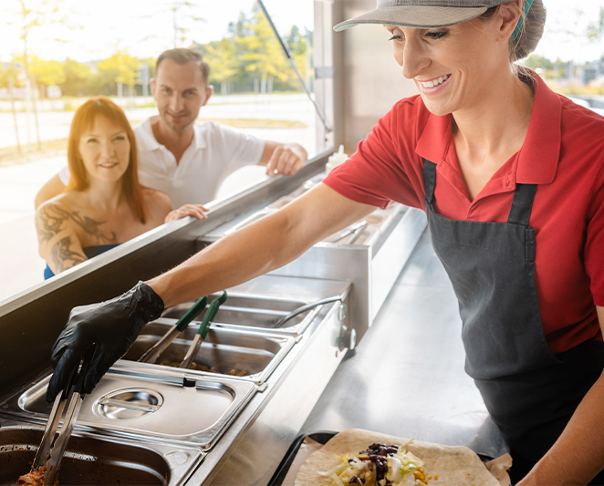 A food prep table, placed in the interior of a food truck is being used by the owner to prepare food.